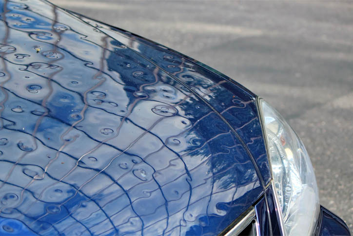 Close up of the top of a royal blue car with tens of dents from hail damage on top.