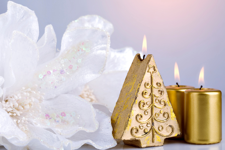 Three golden New Year candles with burning fire standing near delicate white flower on light background.