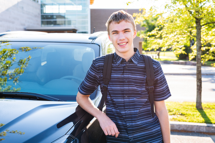 First-time driver and teenager leaning against his car in a high school parking lot.