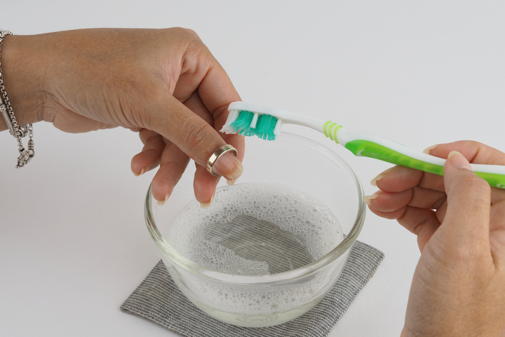 A silver ring being cleaned using a toothbrush and soapy water
