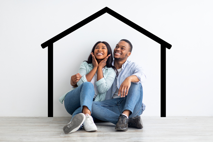 Happy african american spouses sitting near white wall with drawn house, dreaming and imagining their new home, planning relocation, creative collage